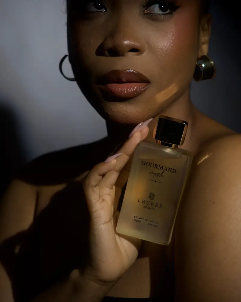 A woman in a dark studio holds Gourmand Rush to her shoulder, then in her fingertips